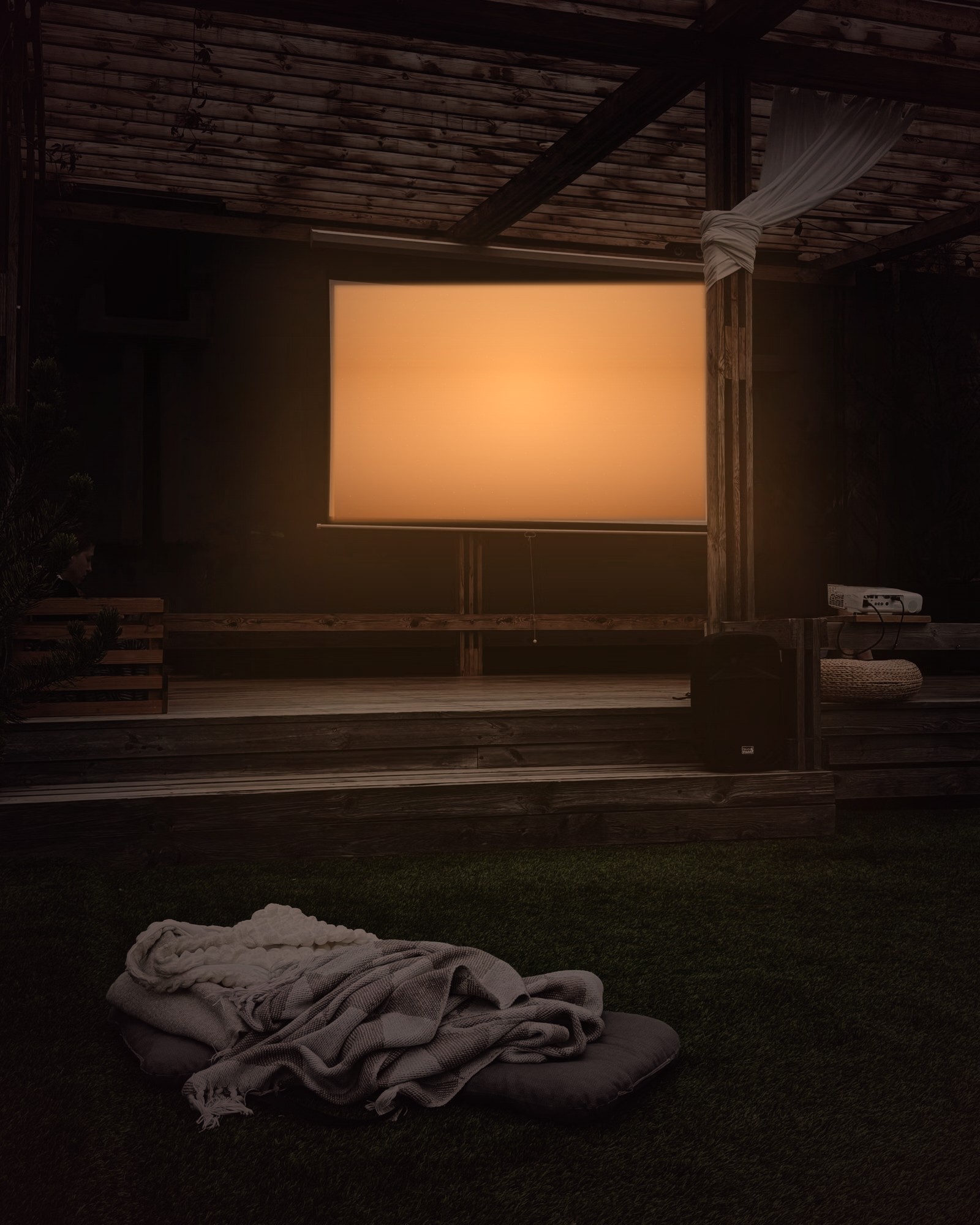 An outdoor cinema at night, the screen glowing warmly above a lawn with a blanket laid out